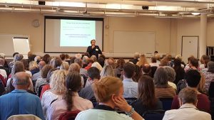 a picture of a lecturer in front of an audience.