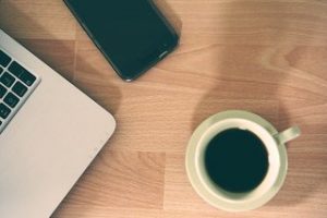 a picture of a coffee on a desk with a laptop and a phone