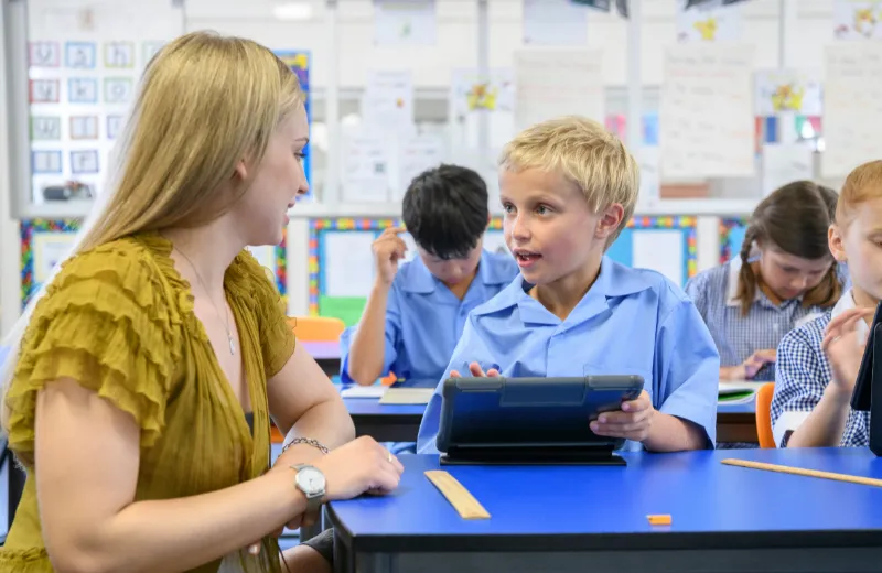 teaching assistant supporting a class of pupils who are using tablets