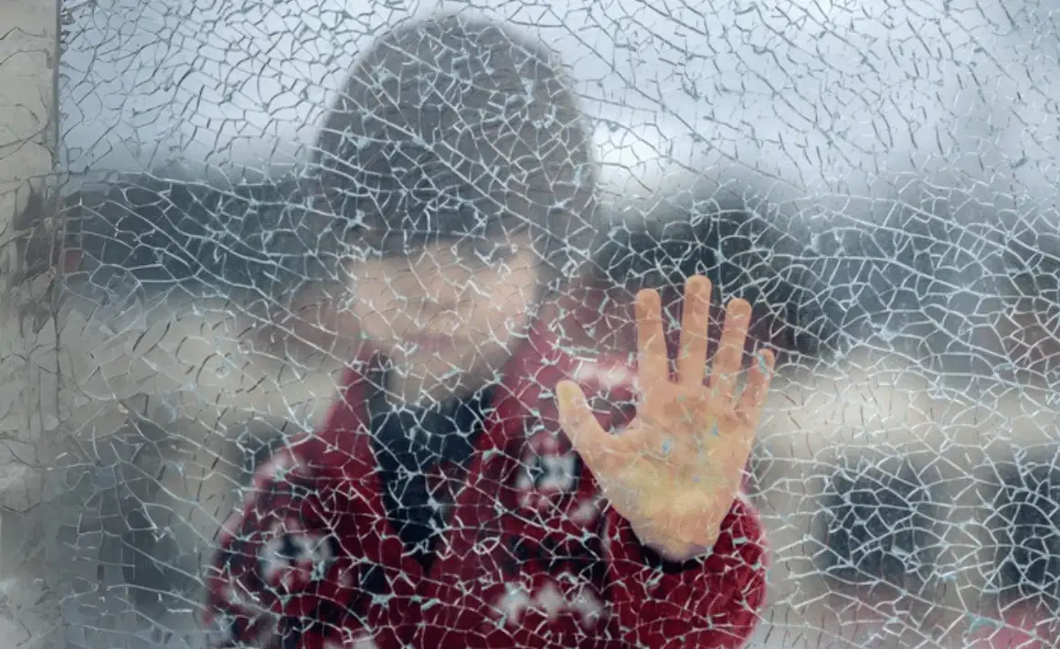 A young child next to a shattered window representing trauma