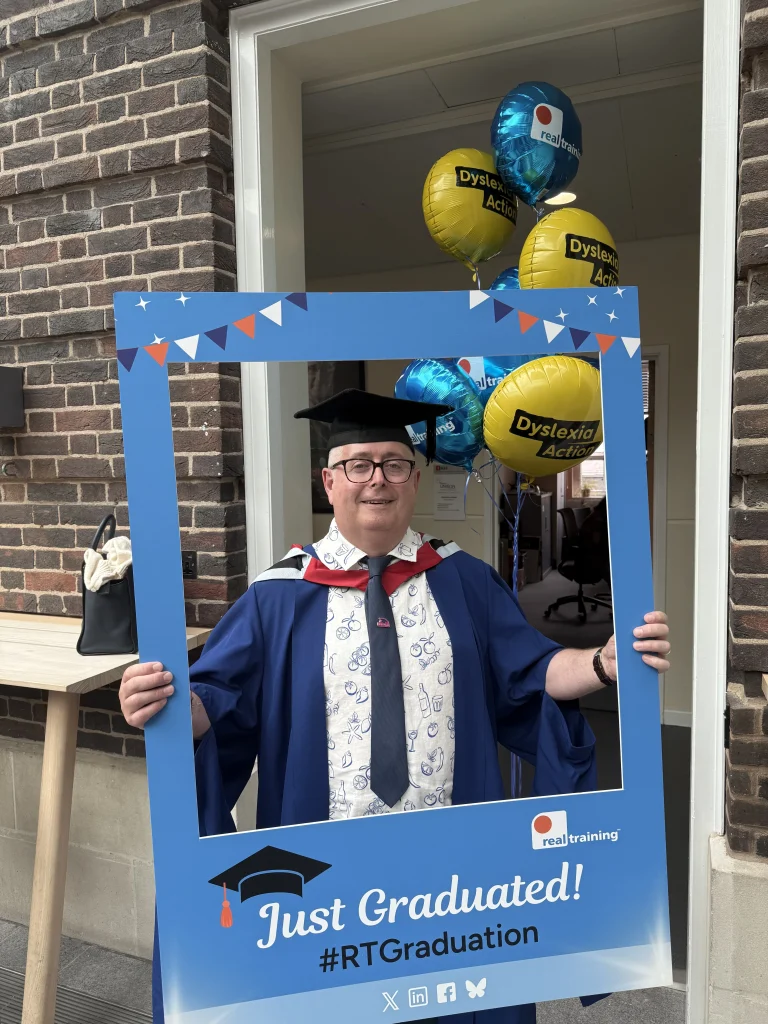 A graduate celebrating with a Real Training selfie frame