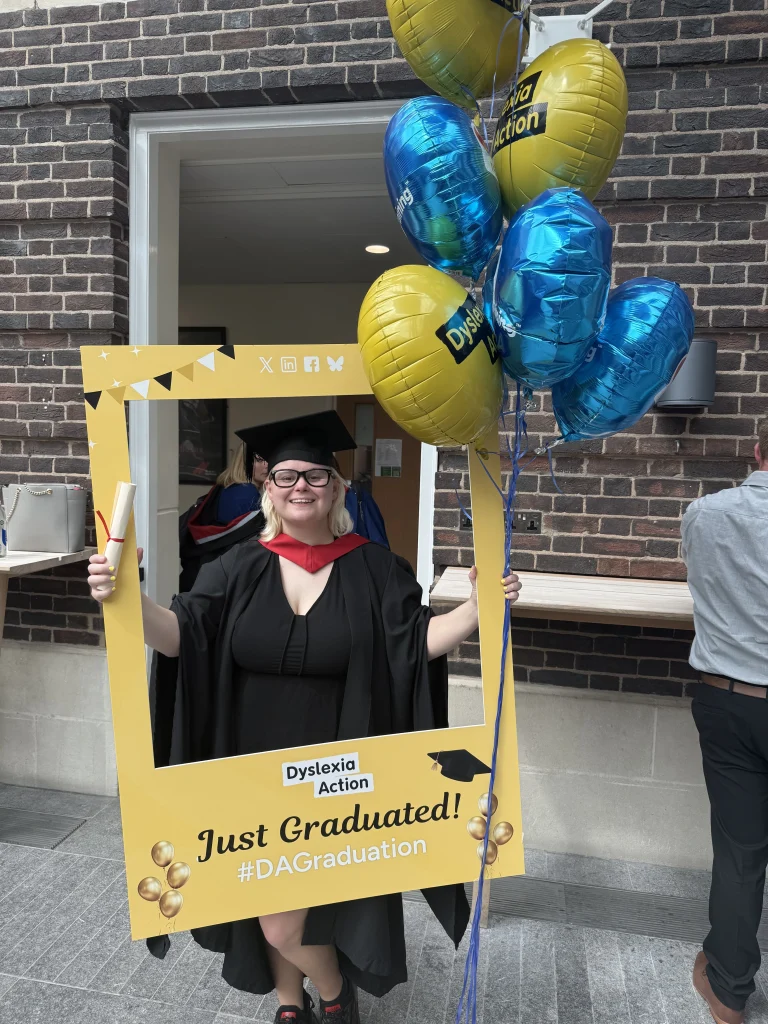 A graduate celebrating with a Dyslexia Action selfie frame