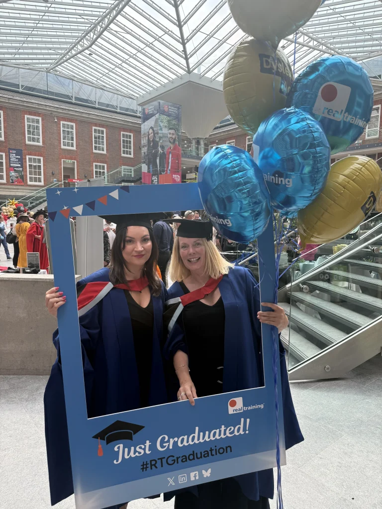 Two graduates celebrating with a Real Training selfie frame